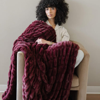 Woman sitting on a chair with Saranoni Double Ruched Faux Fur Throw Blankets Royale draped over her