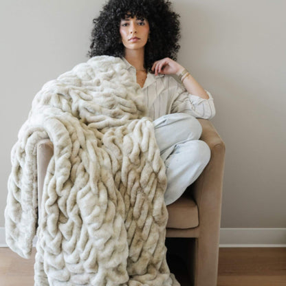Woman sitting on a chair with Saranoni Double Ruched Faux Fur Throw Blankets Sand draped over her