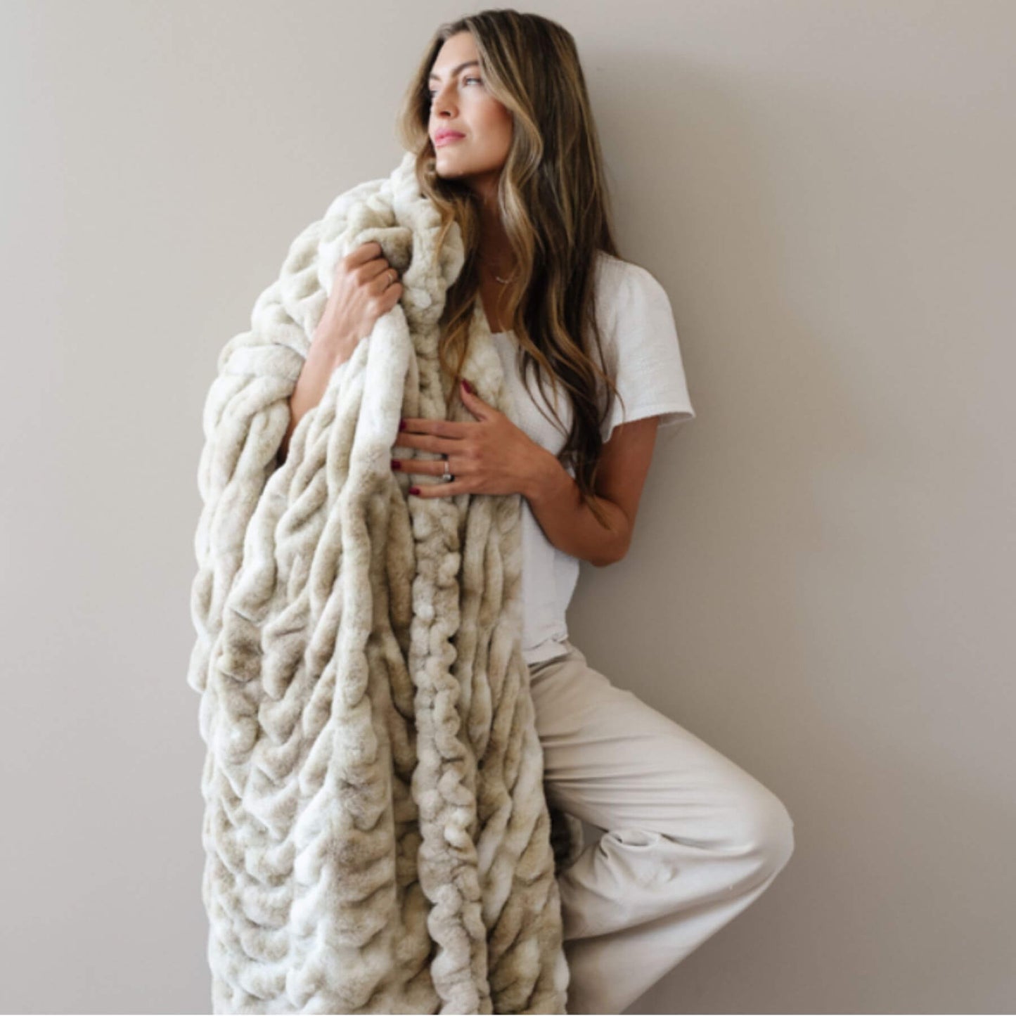 Woman wrapped in Saranoni Double Ruched Faux Fur Throw Blankets Sand against a plain background