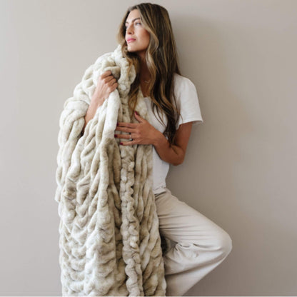 Woman wrapped in Saranoni Double Ruched Faux Fur Throw Blankets Sand against a plain background