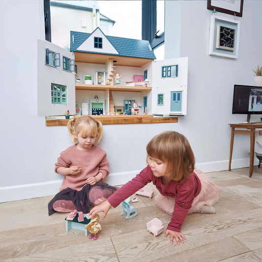 Two children playing with Tender Leaf Dovetail House in a room with a desk and framed pictures.