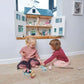 Two children playing with Tender Leaf Dovetail House in a room.