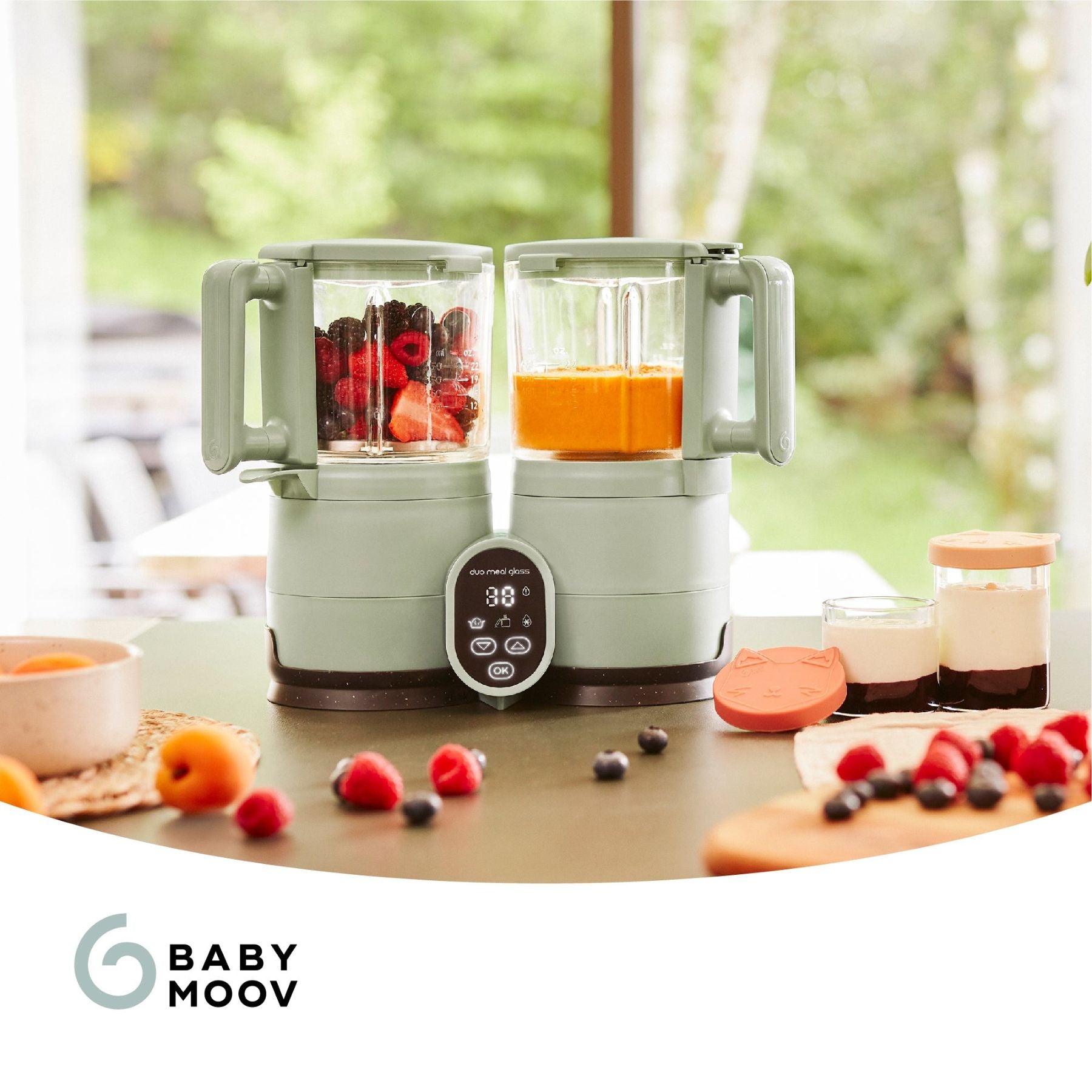Babymoov Duo Meal Glass Pro Baby Food Maker with fruits and a smoothie on a table, featuring the Baby Moov brand.