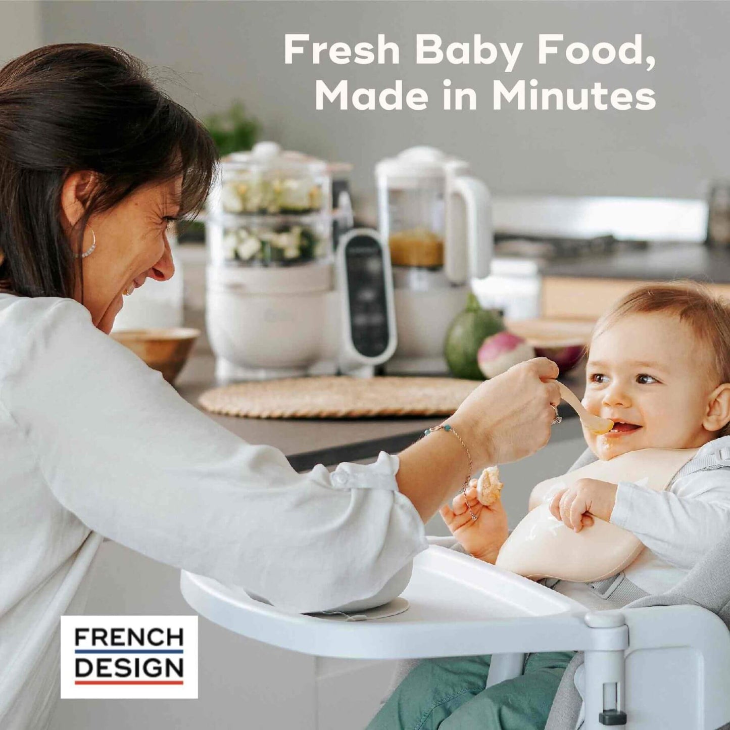 Woman feeding a baby in a high chair with Babymoov Duo Meal Station Baby Food Maker in the background