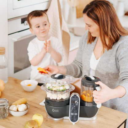 Woman and child in a kitchen with Babymoov Duo Meal Station Baby Food Maker on a counter.