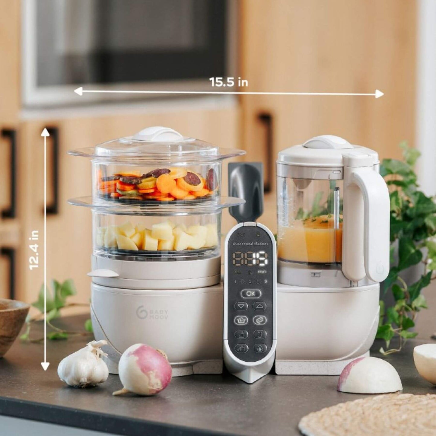 Babymoov Duo Meal Station Baby Food Maker on a countertop, surrounded by vegetables.