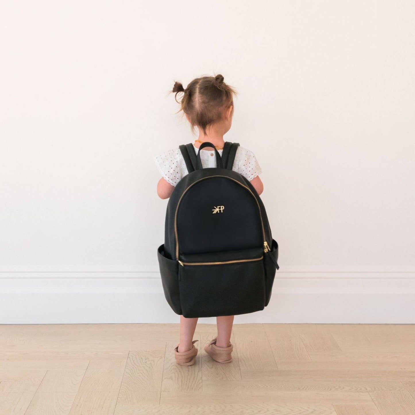 Child wearing a black backpack with a visible brand logo on a plain background