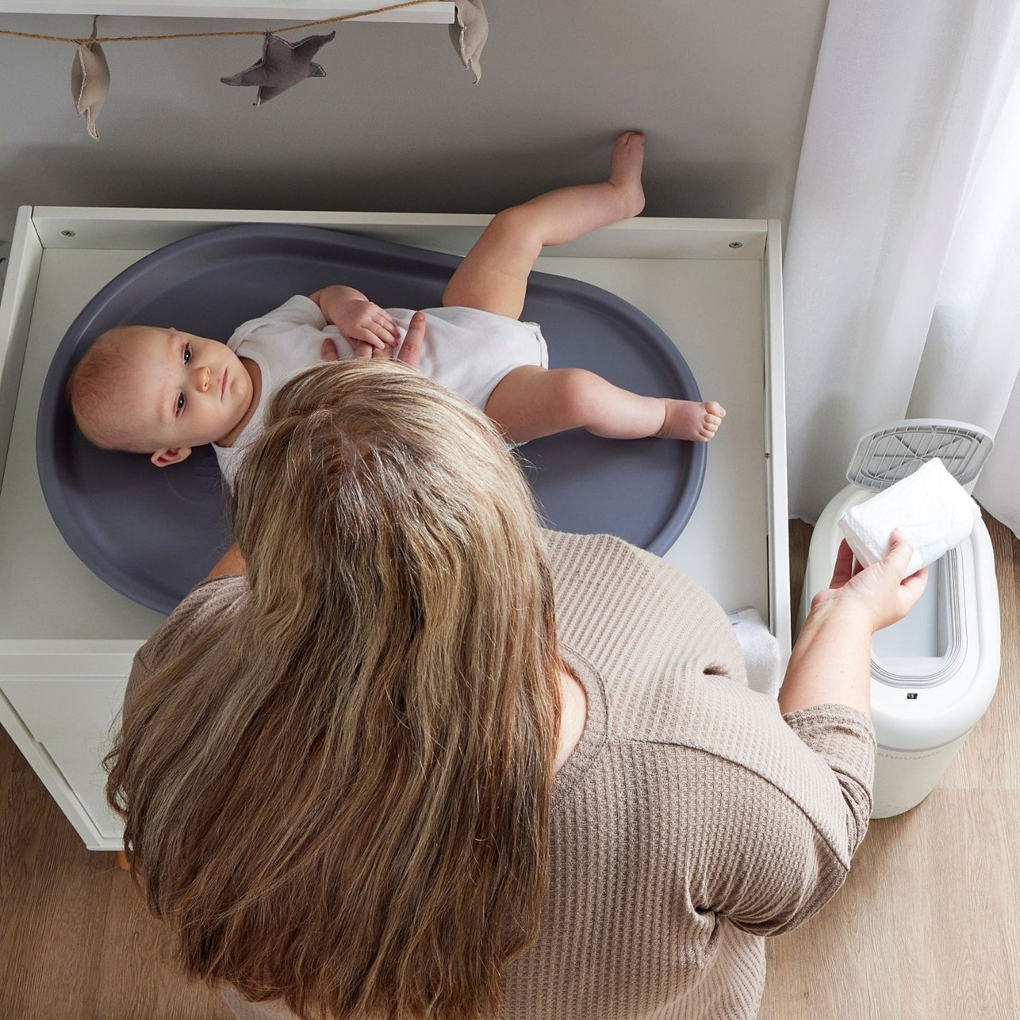 Baby lying in a blue basin with a woman holding a white towel in a bathroom setting.