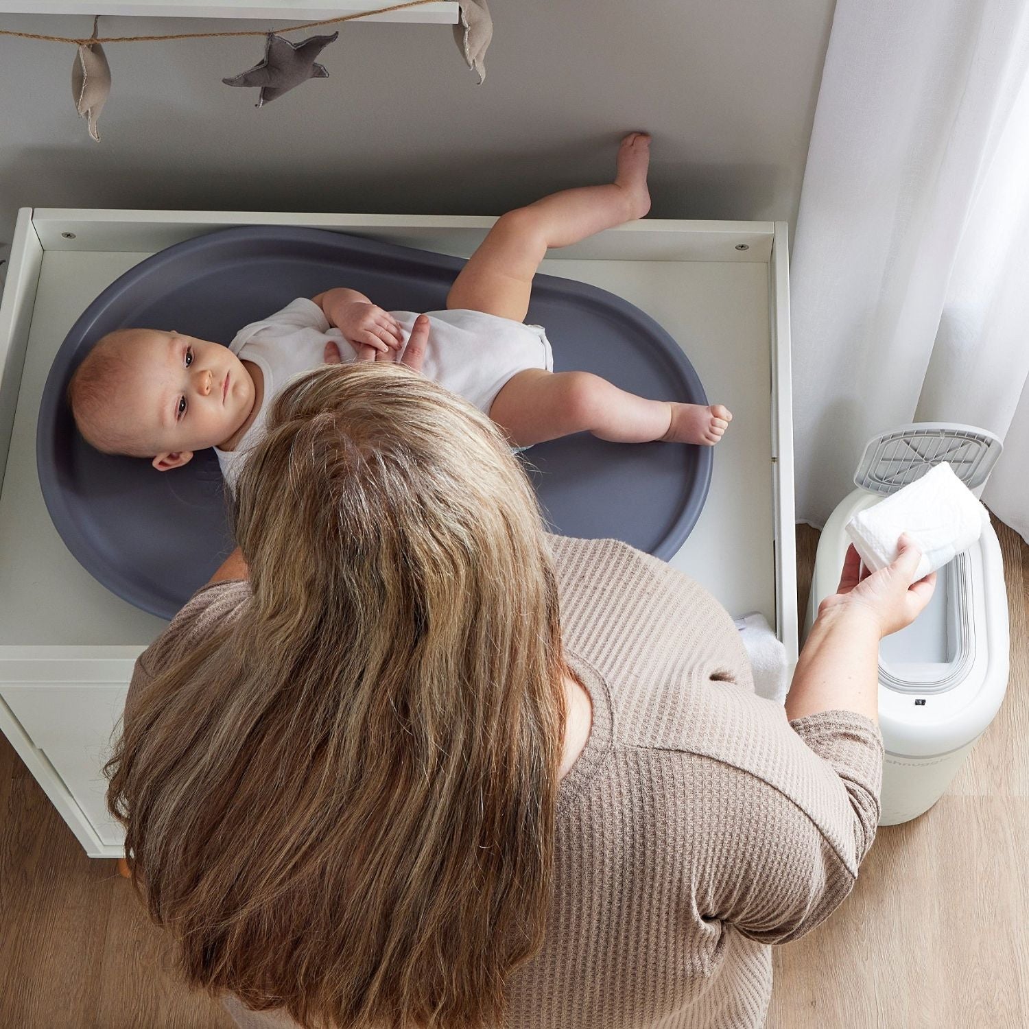 Baby lying in a blue basin with a woman holding a white towel in a bathroom setting.