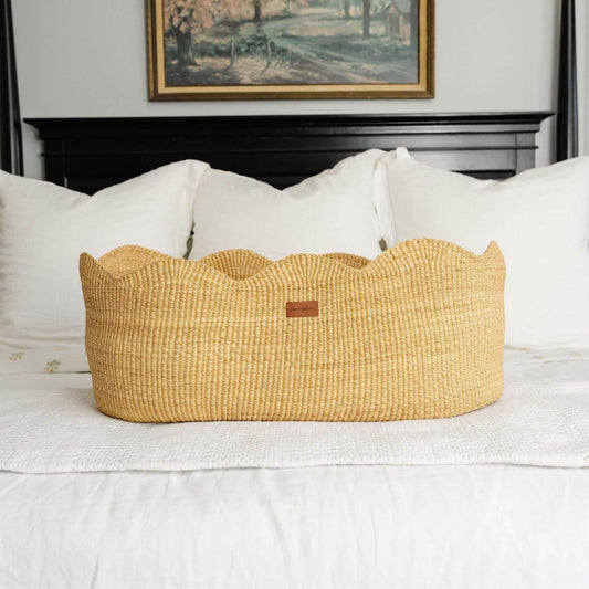 Elaine Bassinet on a bed with white bedding and a framed picture in the background