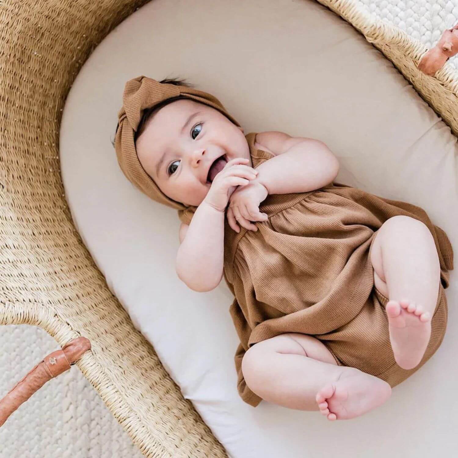 Baby in a brown outfit and headband lying in a woven basket.