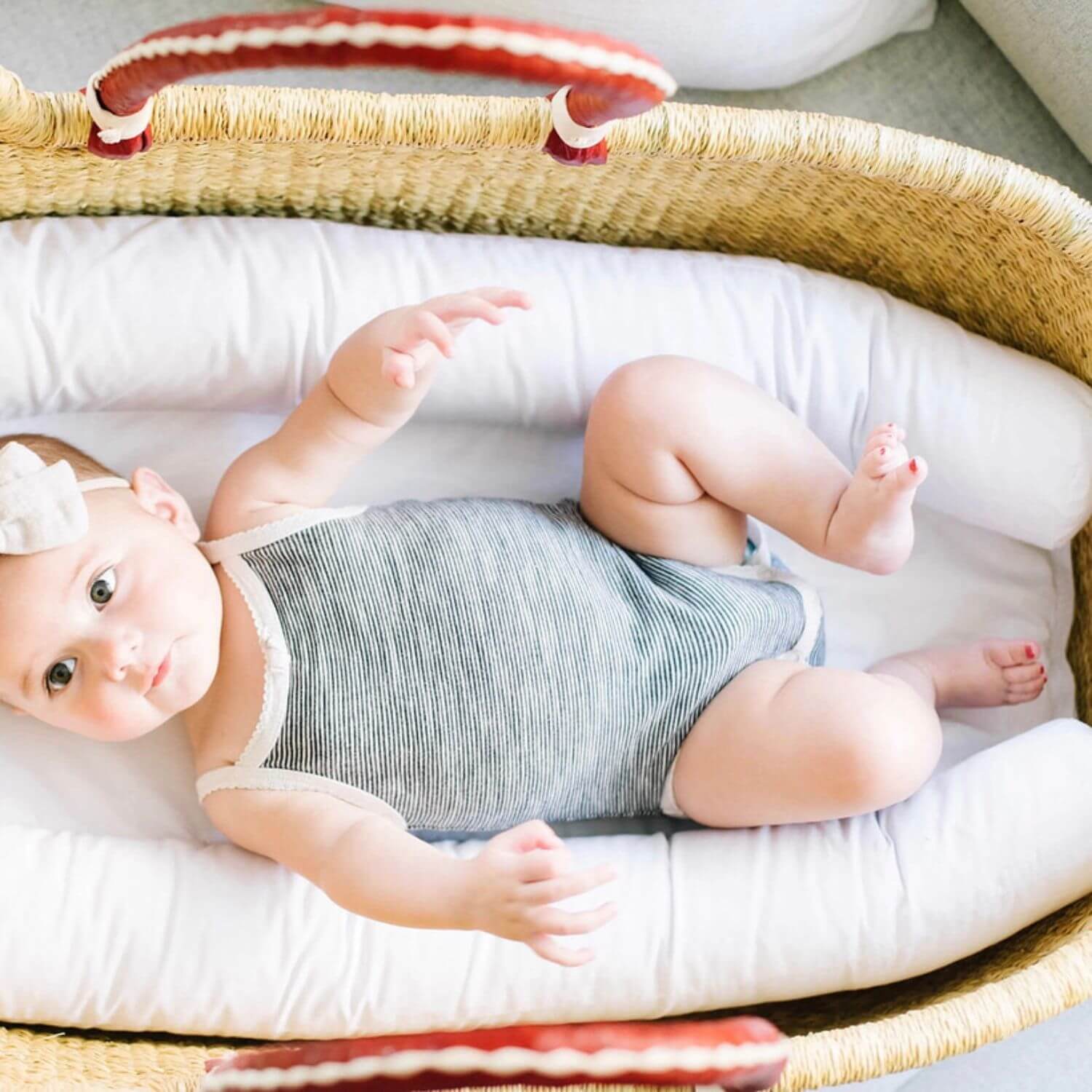 Baby lying in a crib with white bedding and Elaine Bassinet