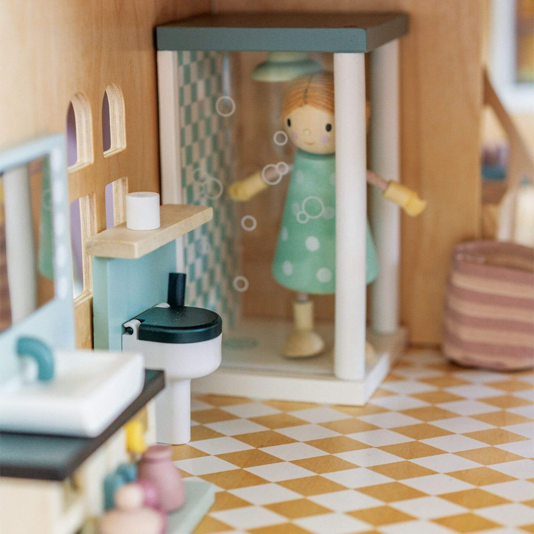 Wooden dollhouse with a doll standing inside, surrounded by furniture and decor.