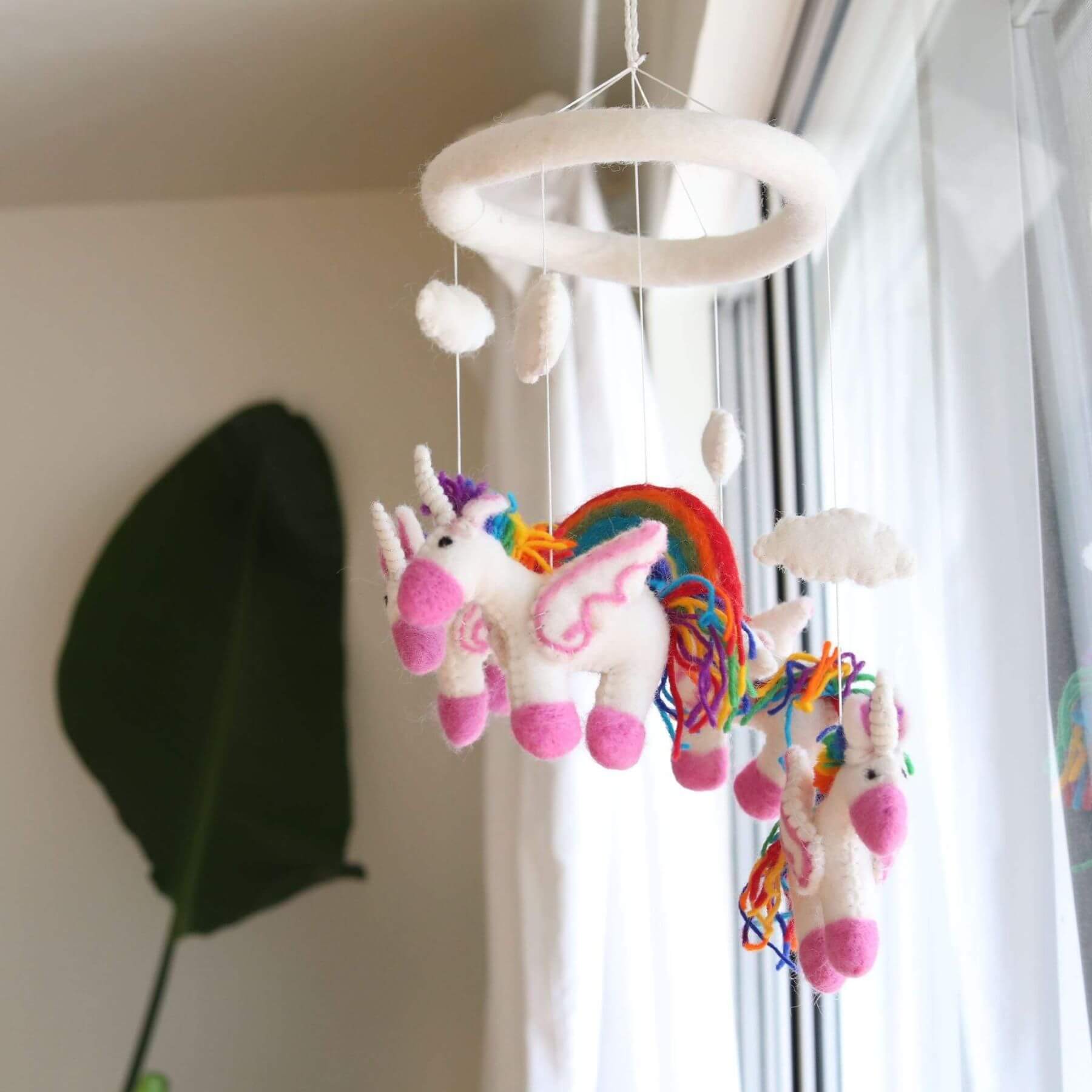 Ganapati Crafts Co. Felt Unicorn Baby Mobile hanging in a room with a window in the background