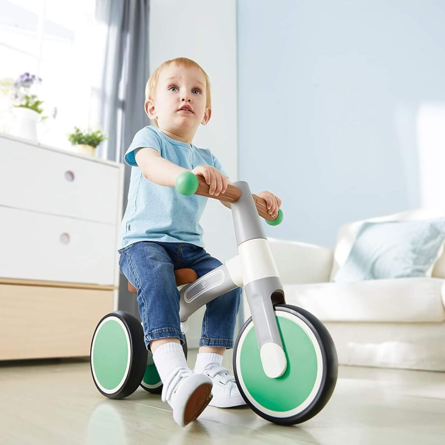 Child riding Hape First Ride Balance Bike Light Green in a room.