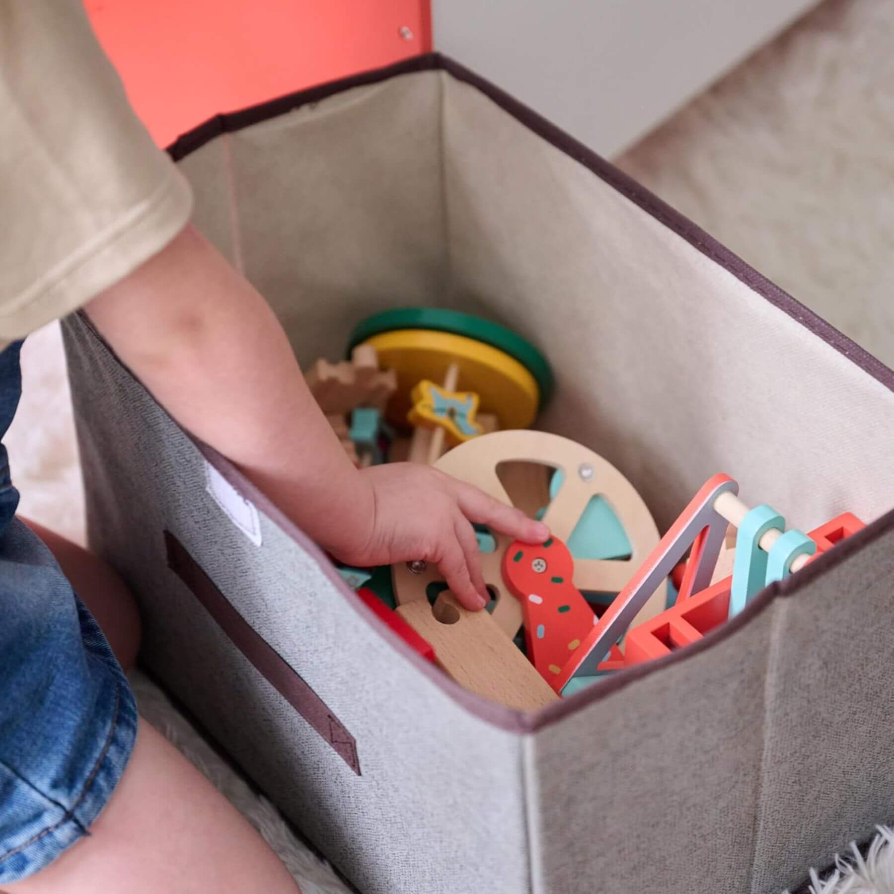 Child playing with colorful wooden toys inside a gray storage bin.