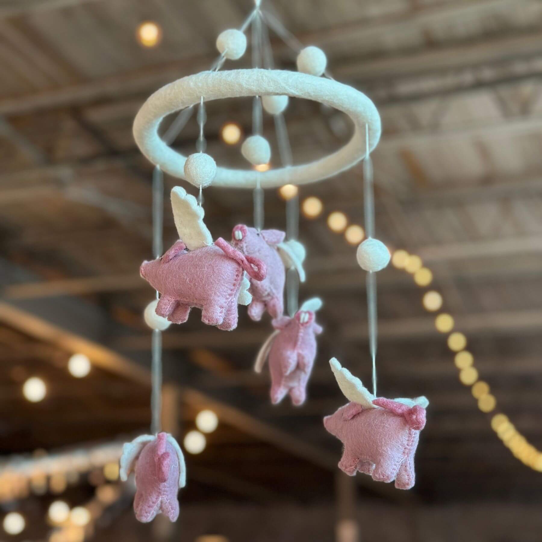 Ganapati Crafts Co. Felt Baby Mobile - Flying Pig hanging from a ceiling with blurred lights in the background