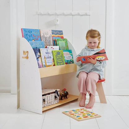 Child reading a book next to Tender Leaf Forest Book Case with books on a white floor.