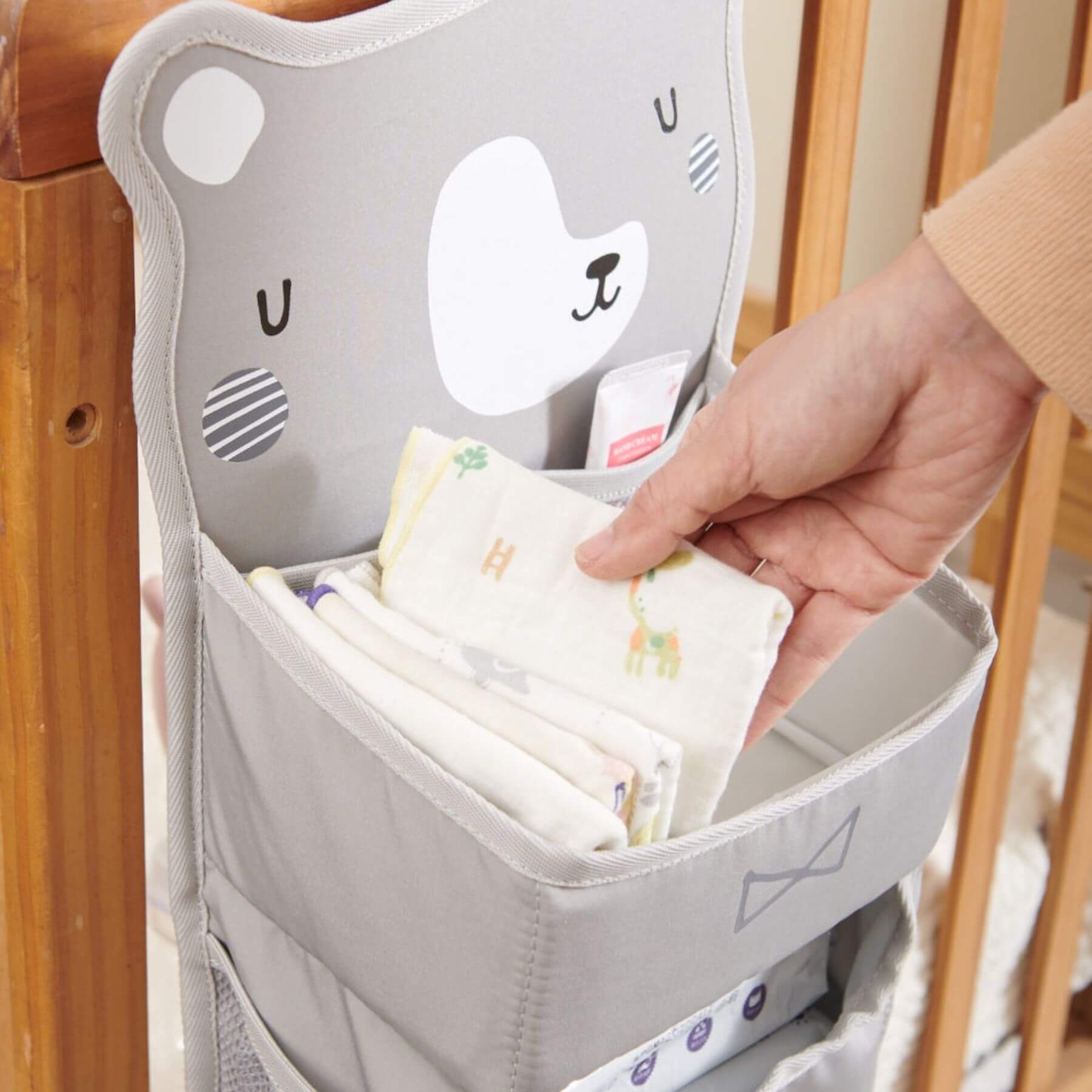 Forest Friends Hanging Organizer bear held by a hand, filled with baby wipes and diapers.