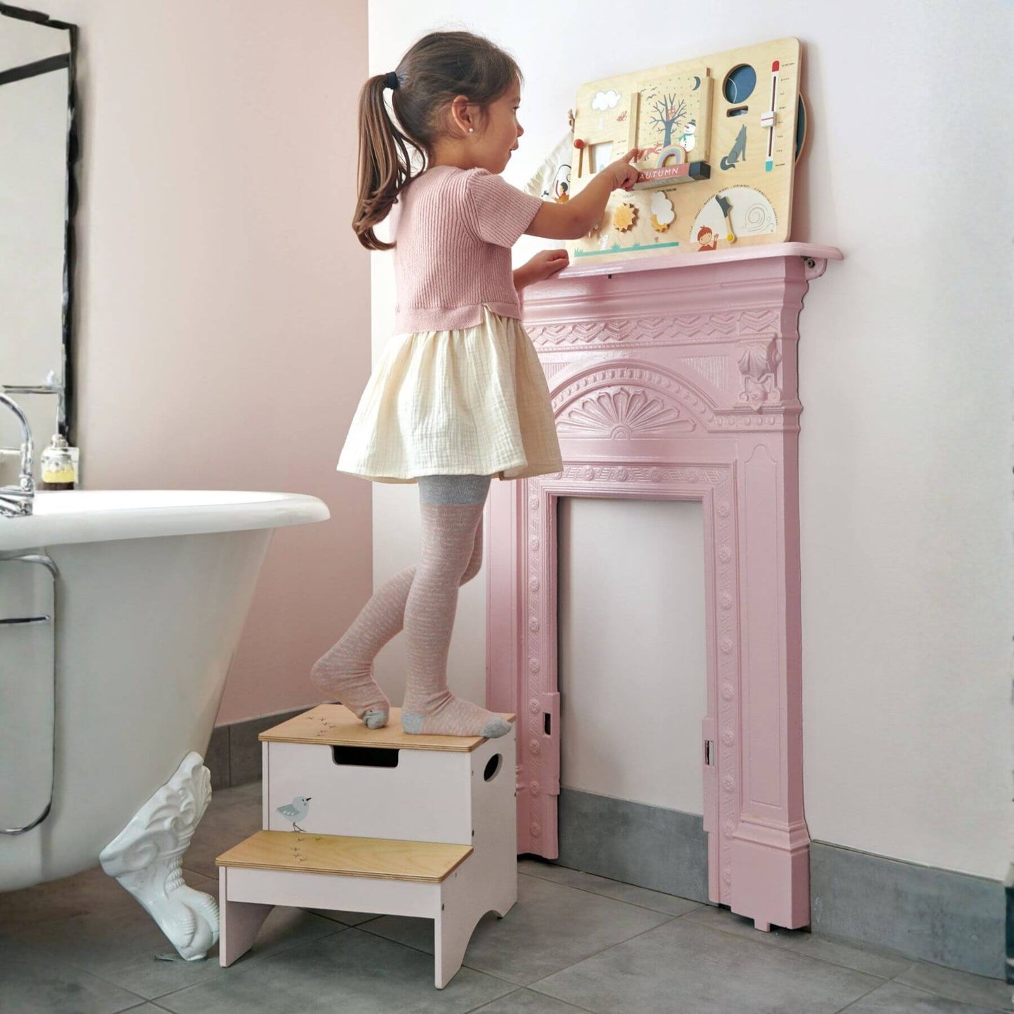 Child using Tender Leaf Forest Steps to reach a toy on a pink fireplace mantle.
