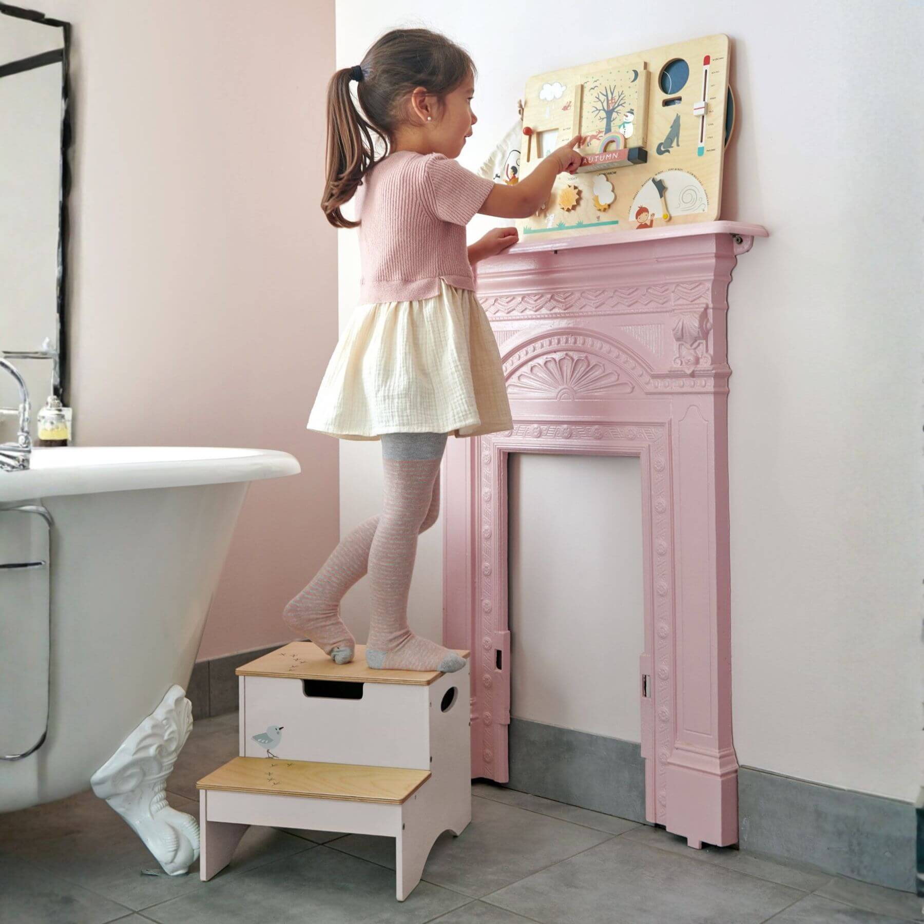 Child using Tender Leaf Forest Steps to reach a toy on a pink fireplace mantle.