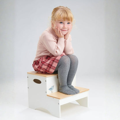 Child sitting on a wooden step stool with a white background