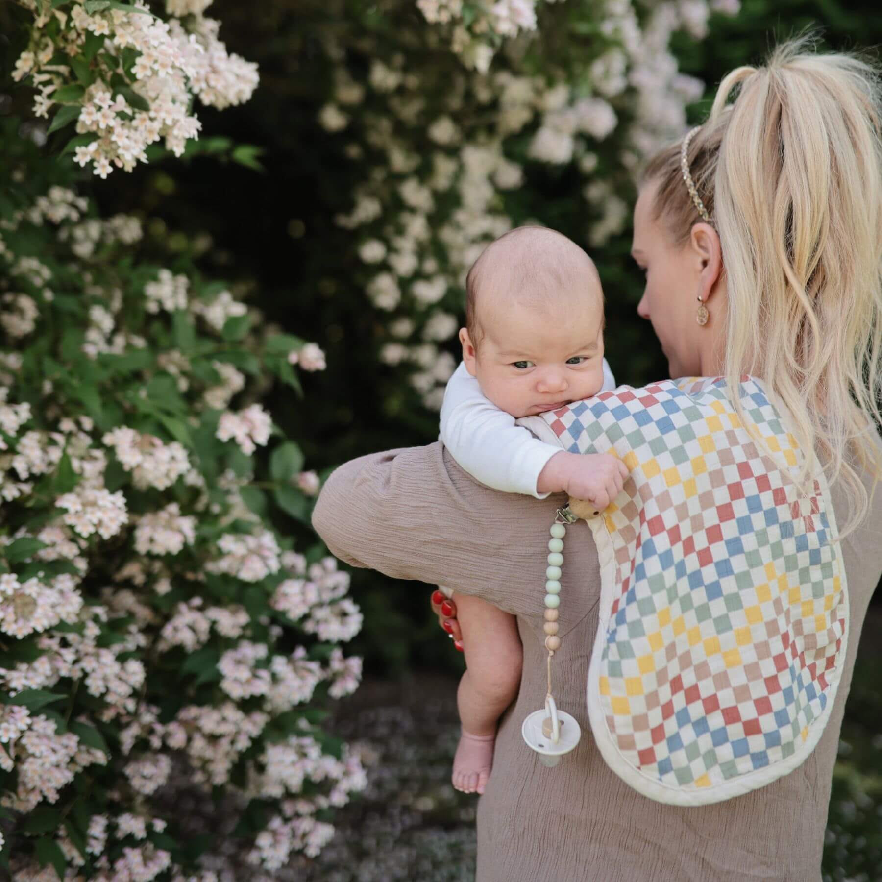 Woman holding a baby wrapped in a colorful blanket with flowers in the background
