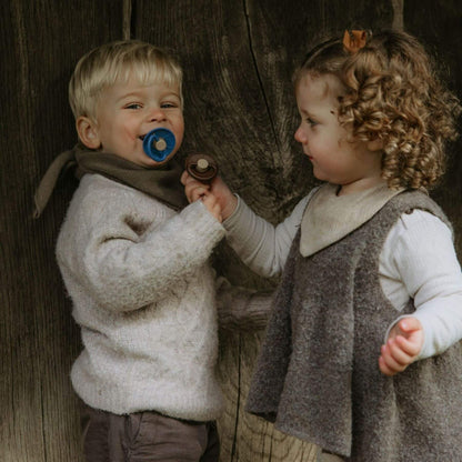 Two children in vintage clothing standing next to a wooden wall.