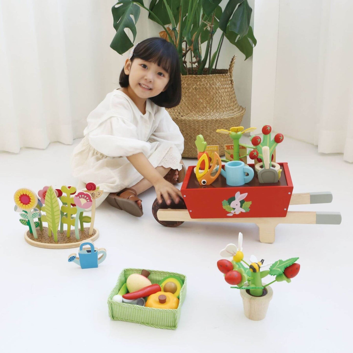 Child playing with Tender Leaf Garden Wheelbarrow Set on a white floor.