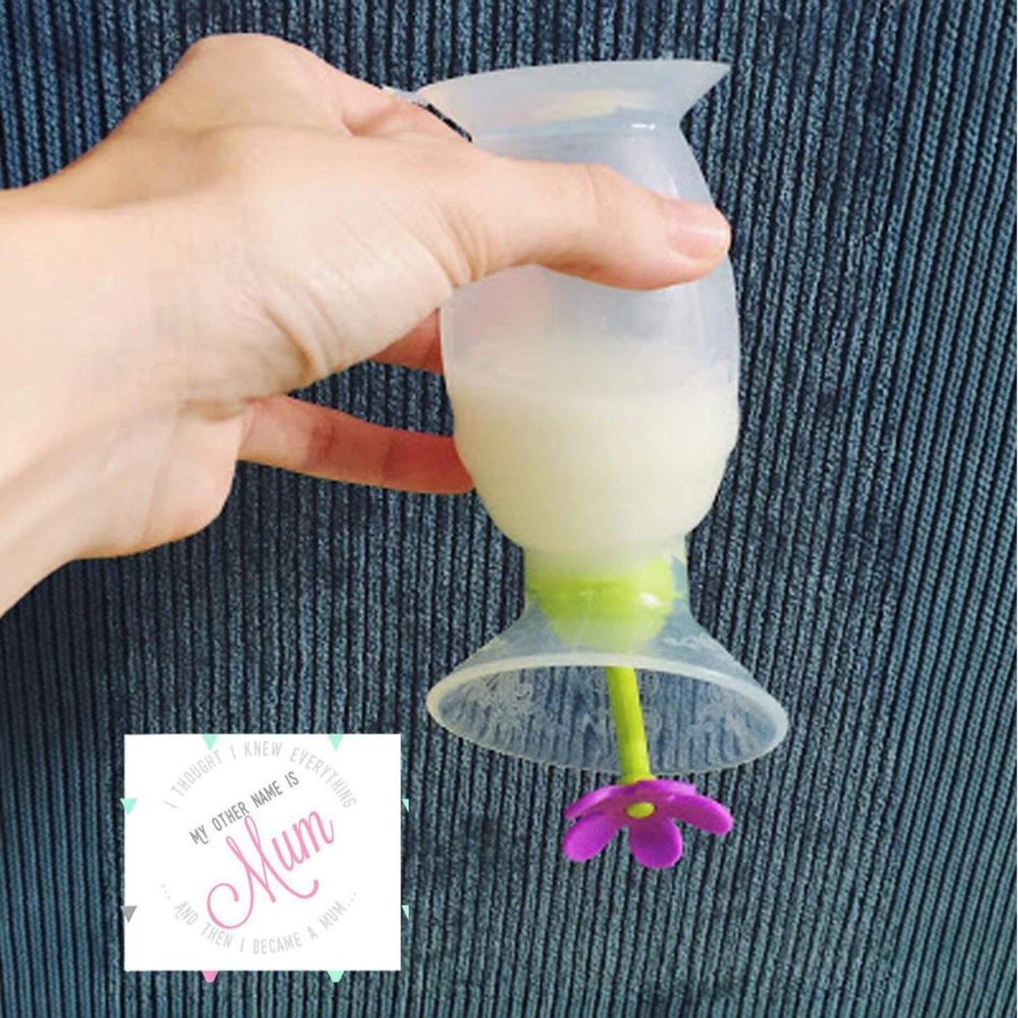 A hand holds a Haakaa Gen 2 Silicone Breast Pump with Suction Base 5 oz and Silicone Flower Stopper Set against a dark ribbed fabric background.