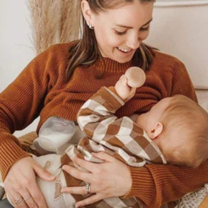 A woman holds a baby. The baby is sucking a wooden teething toy while the woman also using a breast pump
