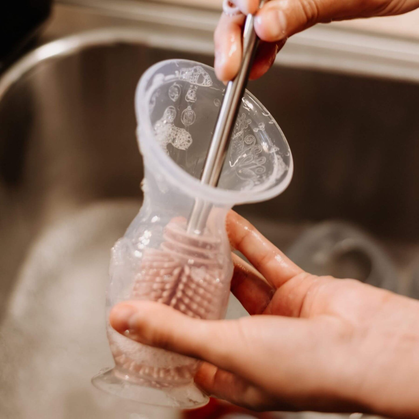 A close-up of a person washing Haakaa Generation 2 Silicone Breast Pump with a brush