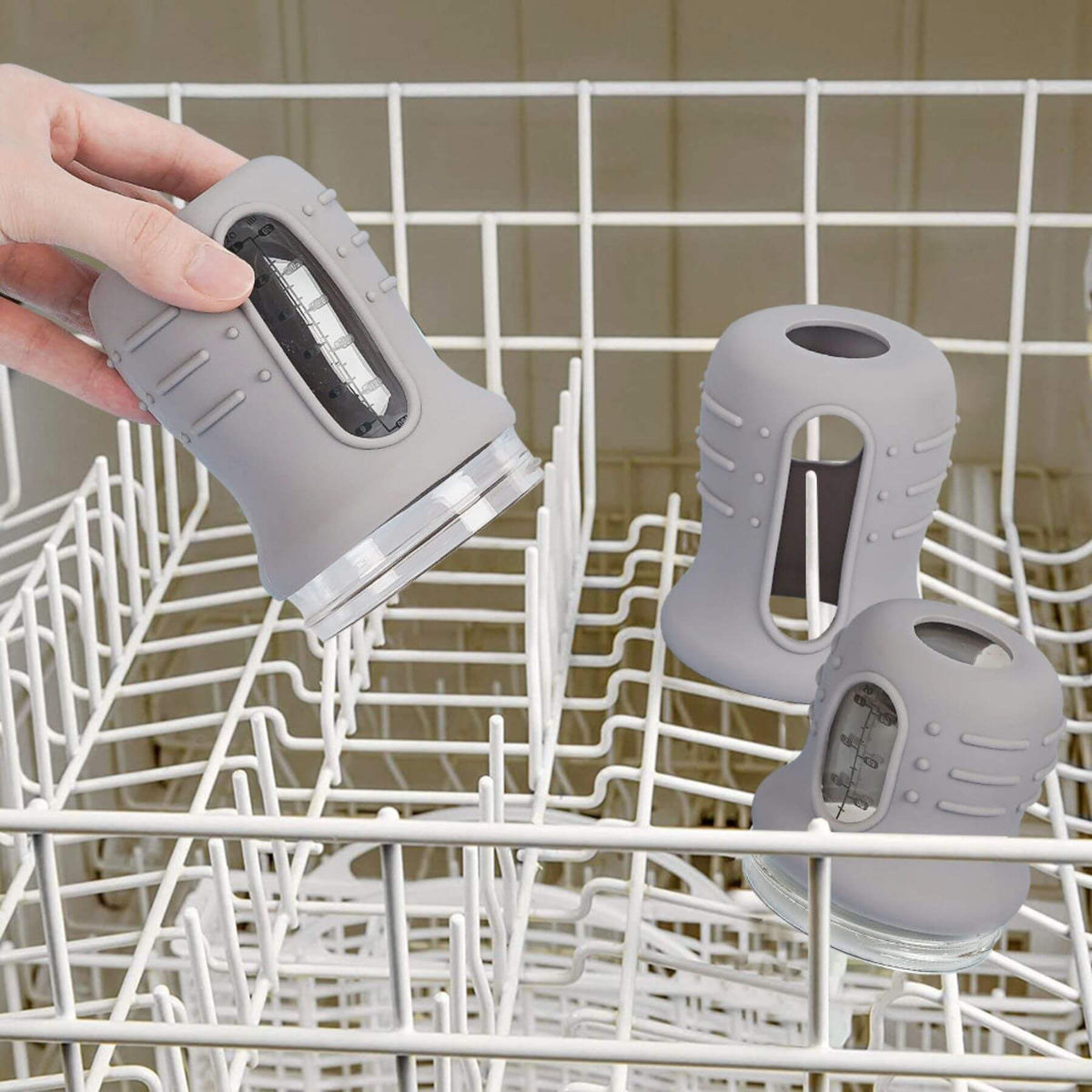A hand is placing baby bottles into a white wire dishwasher rack, with two more matching gray bottles resting inside.