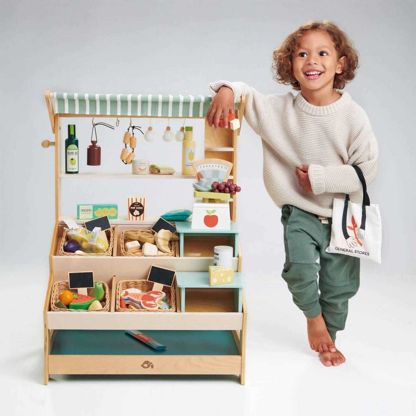 Child standing next to Tender Leaf General Stores with various items on a plain background