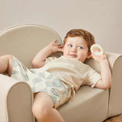 Child lying on Tiny Land® GentleSnug Kid Chair Beige White holding a small object
