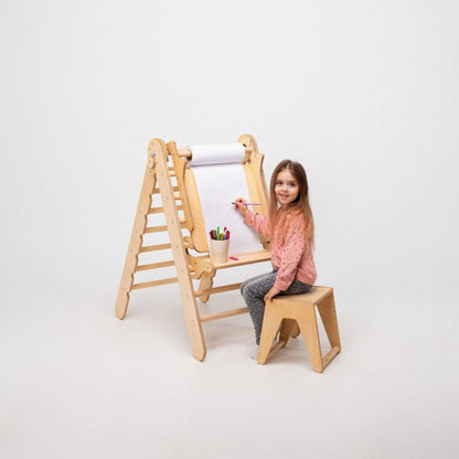 Child sitting on a wooden stool using a drawing board with paper and crayons on a white background