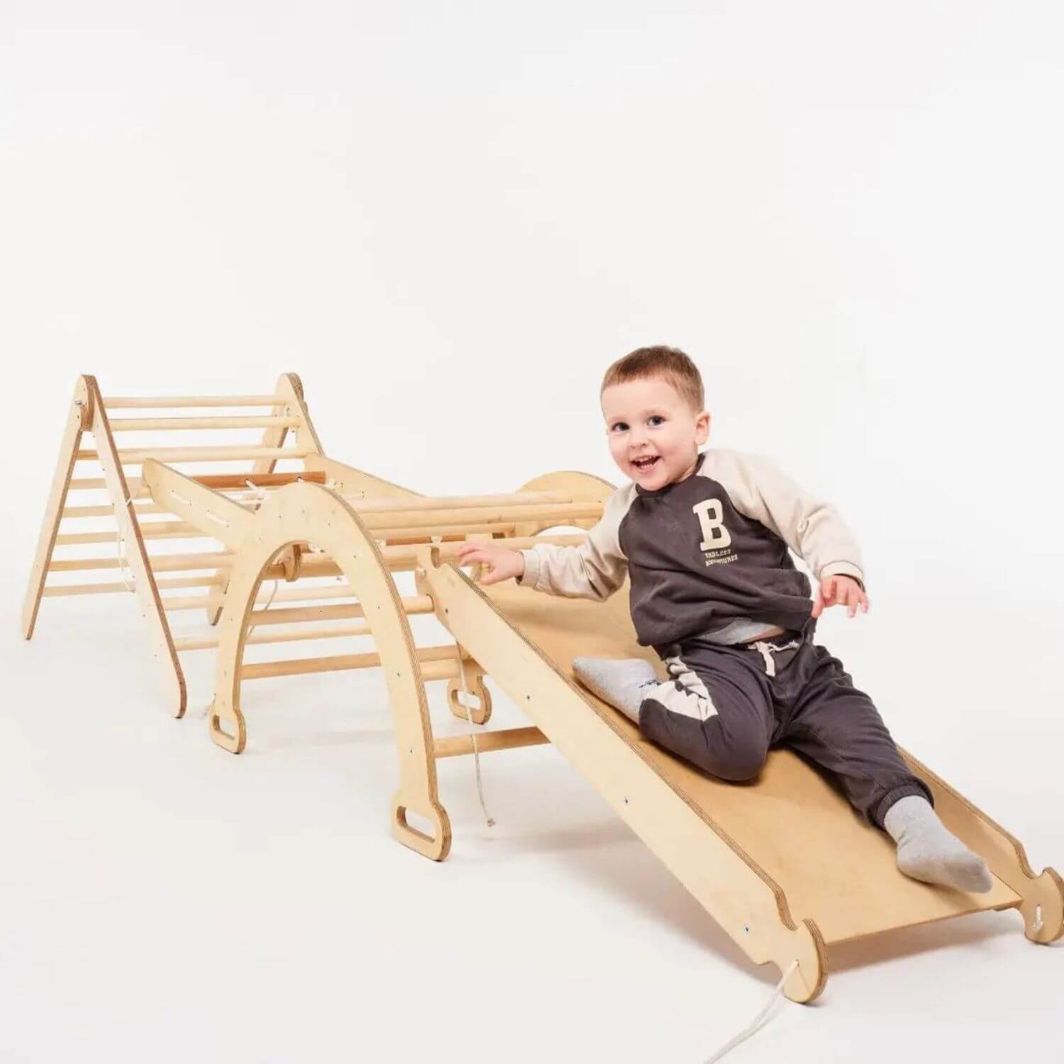 A toddler sits on a light natural wood slide attached to a climbing frame