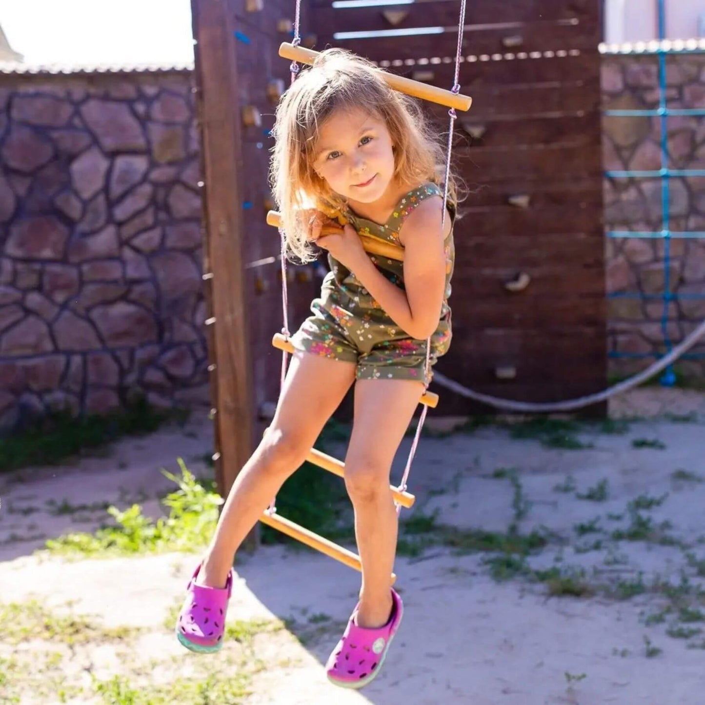 Young girl on Goodevas Climbing Rope Ladder with a stone wall and wooden structure.