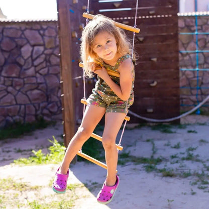 Young girl on Goodevas Climbing Rope Ladder with a stone wall and wooden structure.