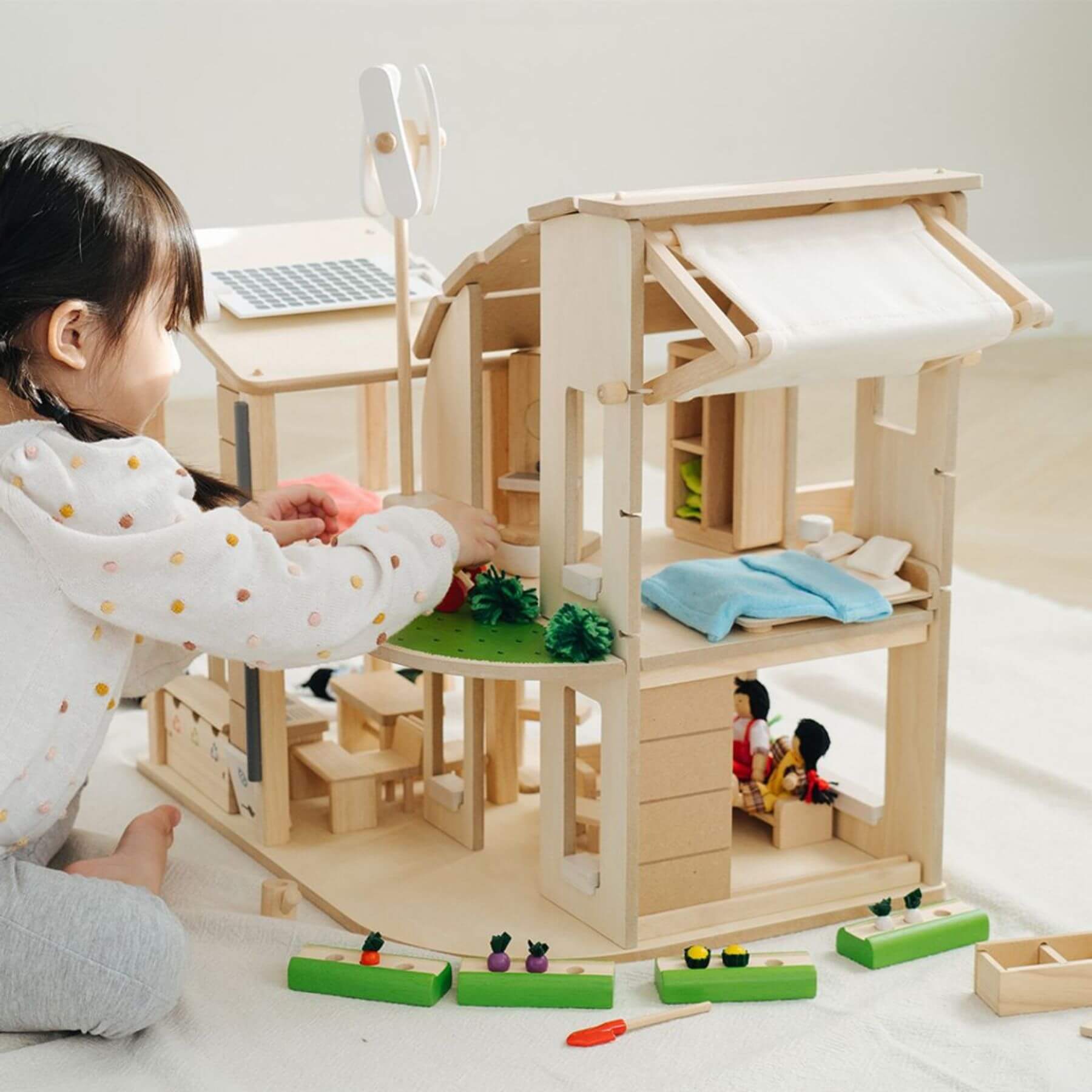 Child playing with PlanToys Green Dollhouse With Furniture on a light-colored floor.