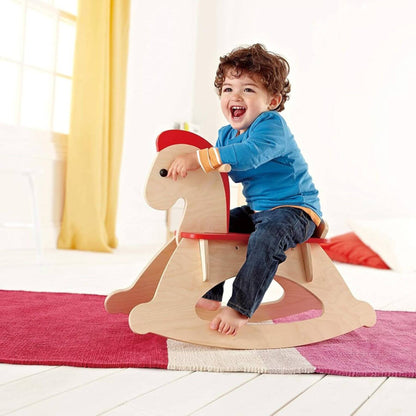 Child sitting on Hape Grow-with-me Rocking Horse in a bright room with yellow curtains.