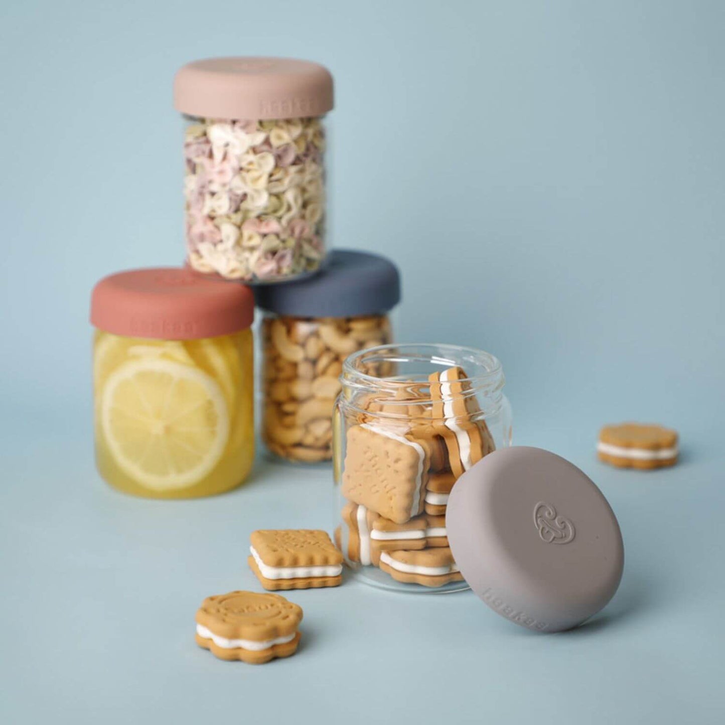 Haakaa Sealed Glass Storage Jar Set containing cookies, a lemonade glass, and loose sandwich cookies on a light blue background.