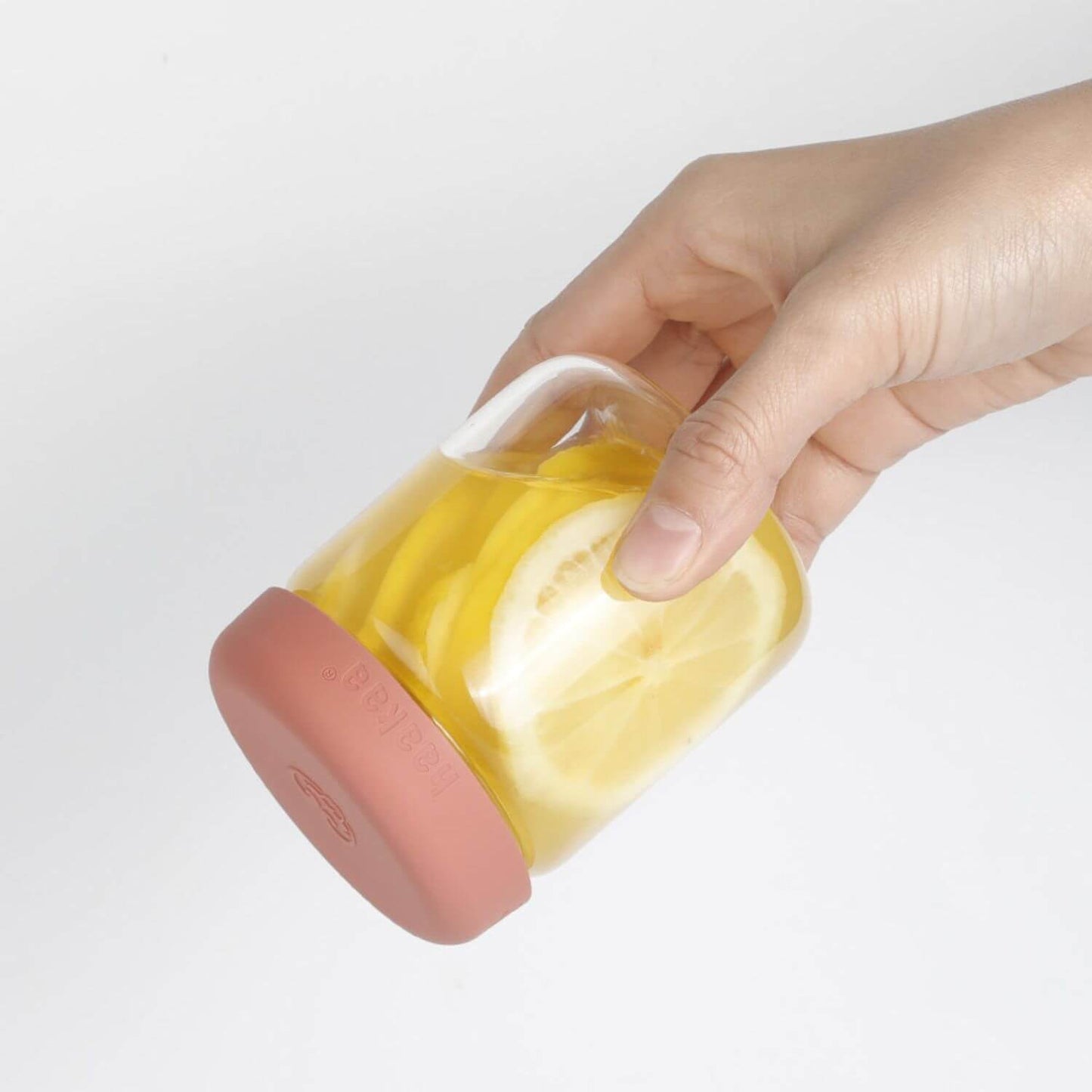 Hand holding Haakaa Sealed Glass Storage Jar with yellow fruit on a light gray background