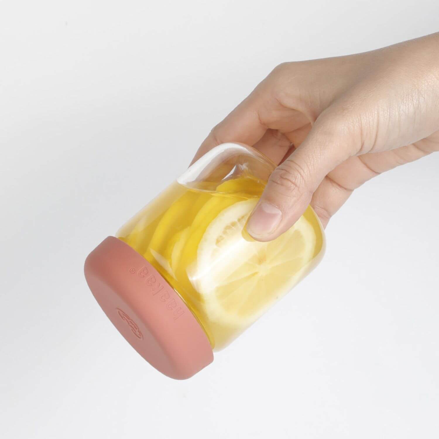 Hand holding Haakaa Sealed Glass Storage Jar with yellow fruit on a light gray background