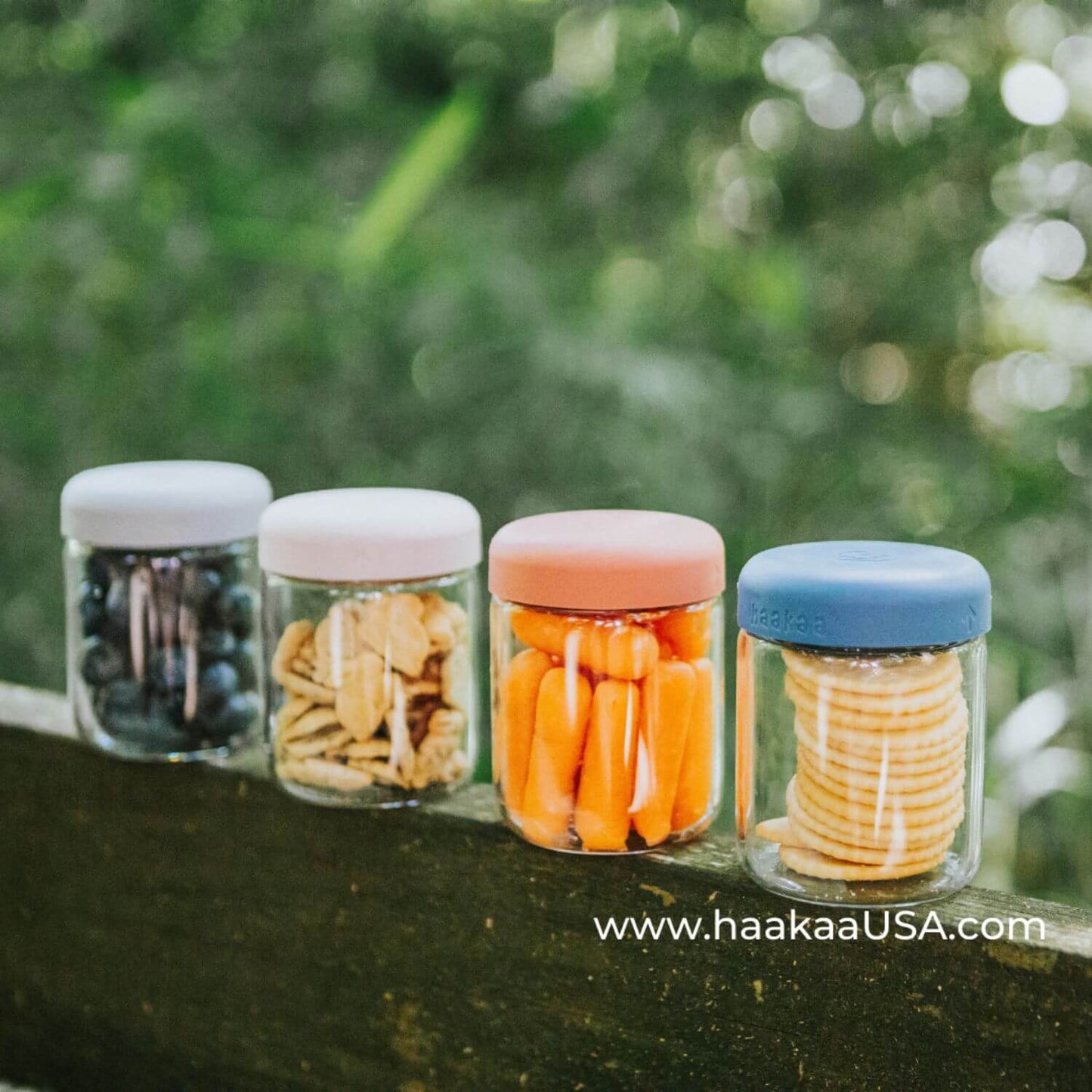 Four Haakaa Sealed Glass Storage Jar Set containing snacks on a natural background