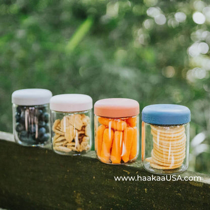 Four Haakaa Sealed Glass Storage Jar Set containing snacks on a natural background
