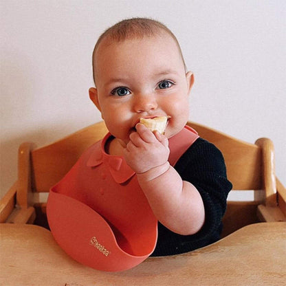 Baby in a high chair wearing a red bib eating a piece of food.