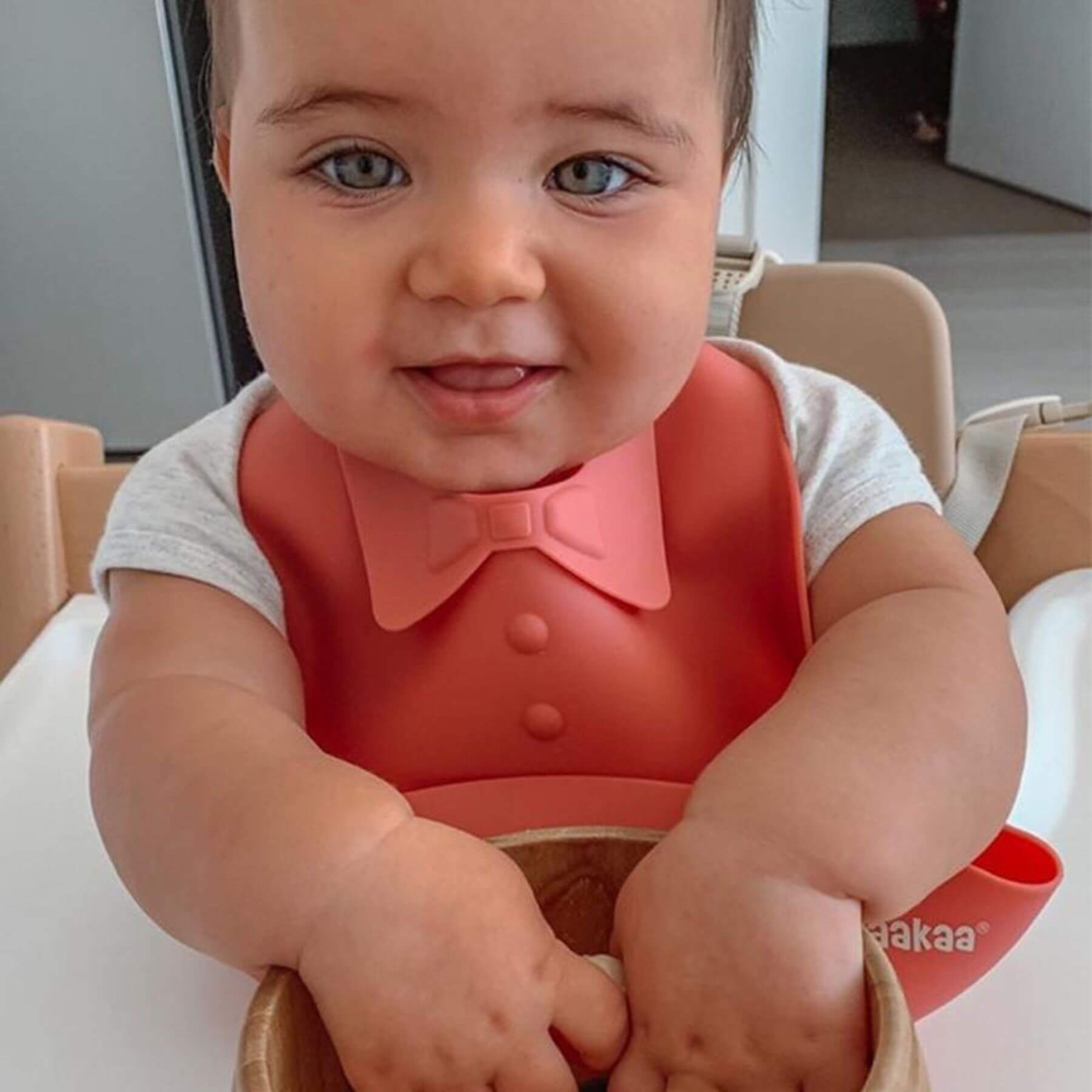 Child wearing a red bib with a bow tie, sitting in a high chair.