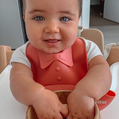 Child wearing a red bib with a bow tie, sitting in a high chair.