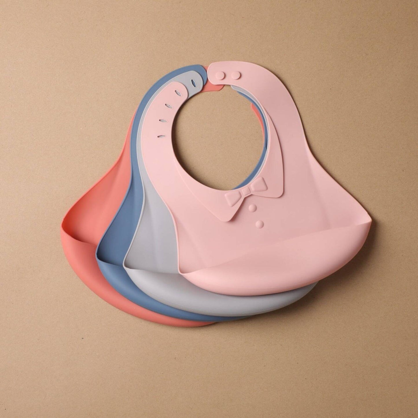 Stack of pink, blue, and gray baby bibs on a beige background